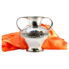 Olla de plata con dos asas entrelazadas con relieves florales y frisos en la base