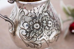 Silver pot with raised floral motifs, monogram card, and question-mark handle