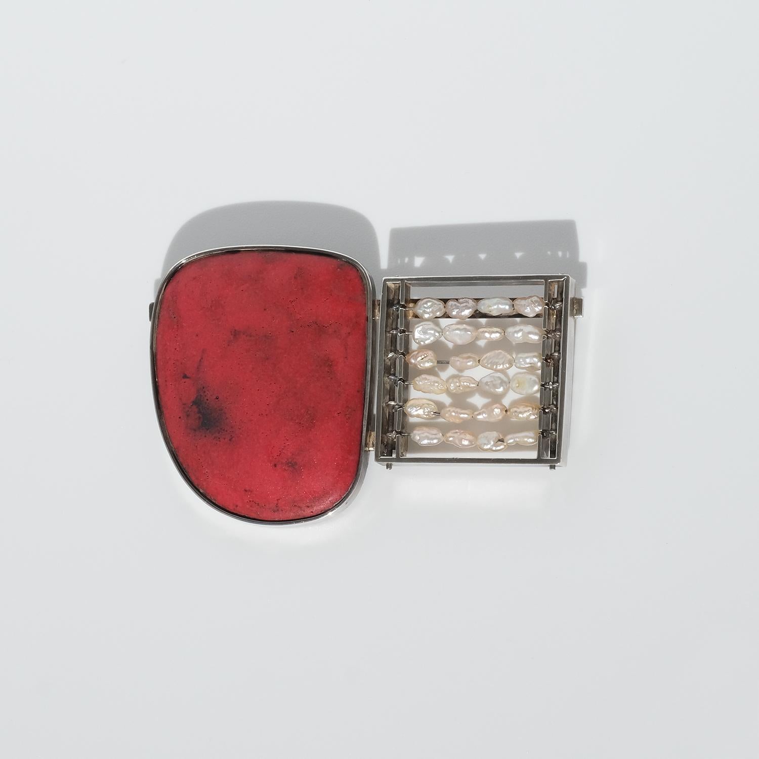 This brooch is adorned with an asymmetric red stone and a square that contains beads strung on wire.

This unusual creation is what we would call a happy item and it can easily be categorized as a conversation piece. It is a piece of art.