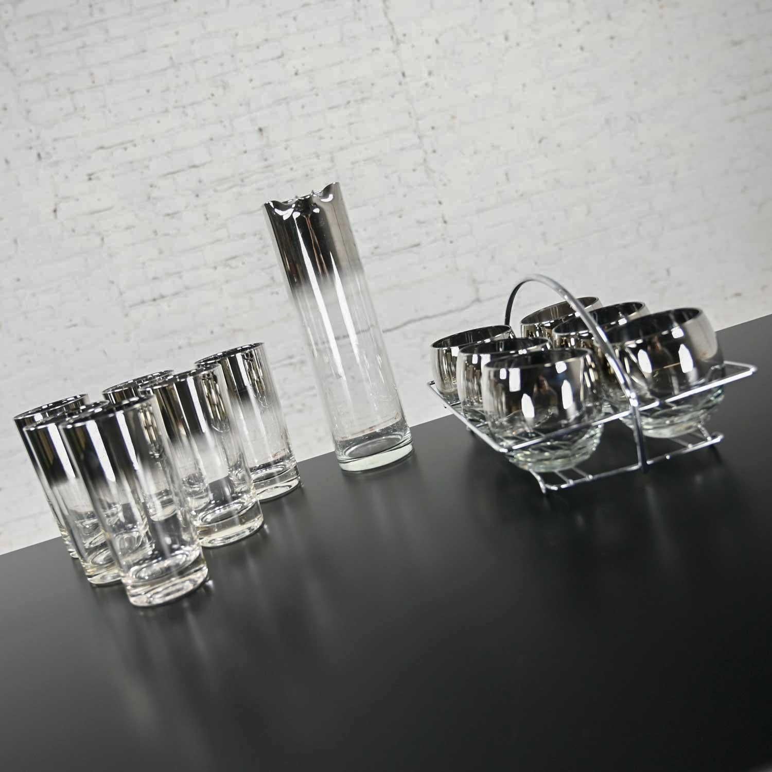 Stunning vintage silver rimmed ombre 14-piece cocktail glassware set attributed to Dorothy Thorpe. The set is comprised of six roly poly glasses in a chrome caddy with handle, 6 Tom Collins glasses, and a handle less cocktail pitcher or carafe.