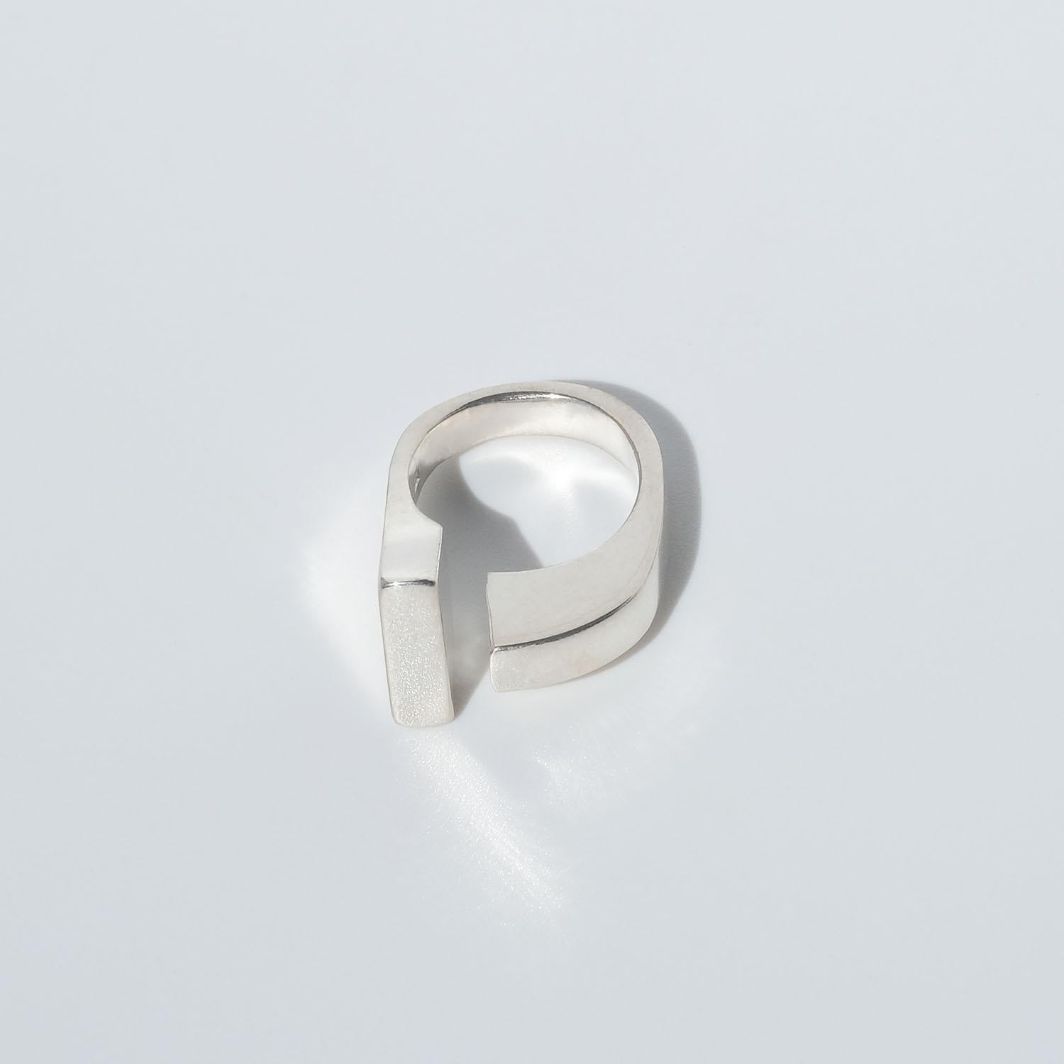 This silver ring has a glossy surface and an asymmetrical shape, with an open top. One side is arched, whilst the other is straight.

The ring has a modern appearance and will, depending on your preference and finger size, look just as good on a