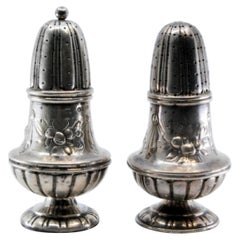 Silver salt and pepper shakers with raised plant elements and a knob on the lid