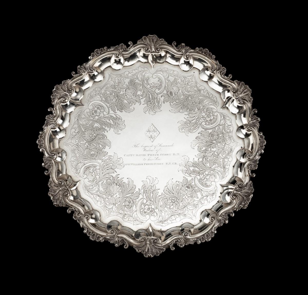 A William IV silver salver with shellwork and scroll border, on four feet, profusely chased and engraved with foliate decoration and inscribed in the centre beneath a widow’s coat of arms: The bequest of Susannah Widow of Captn David Pryce Cumby
