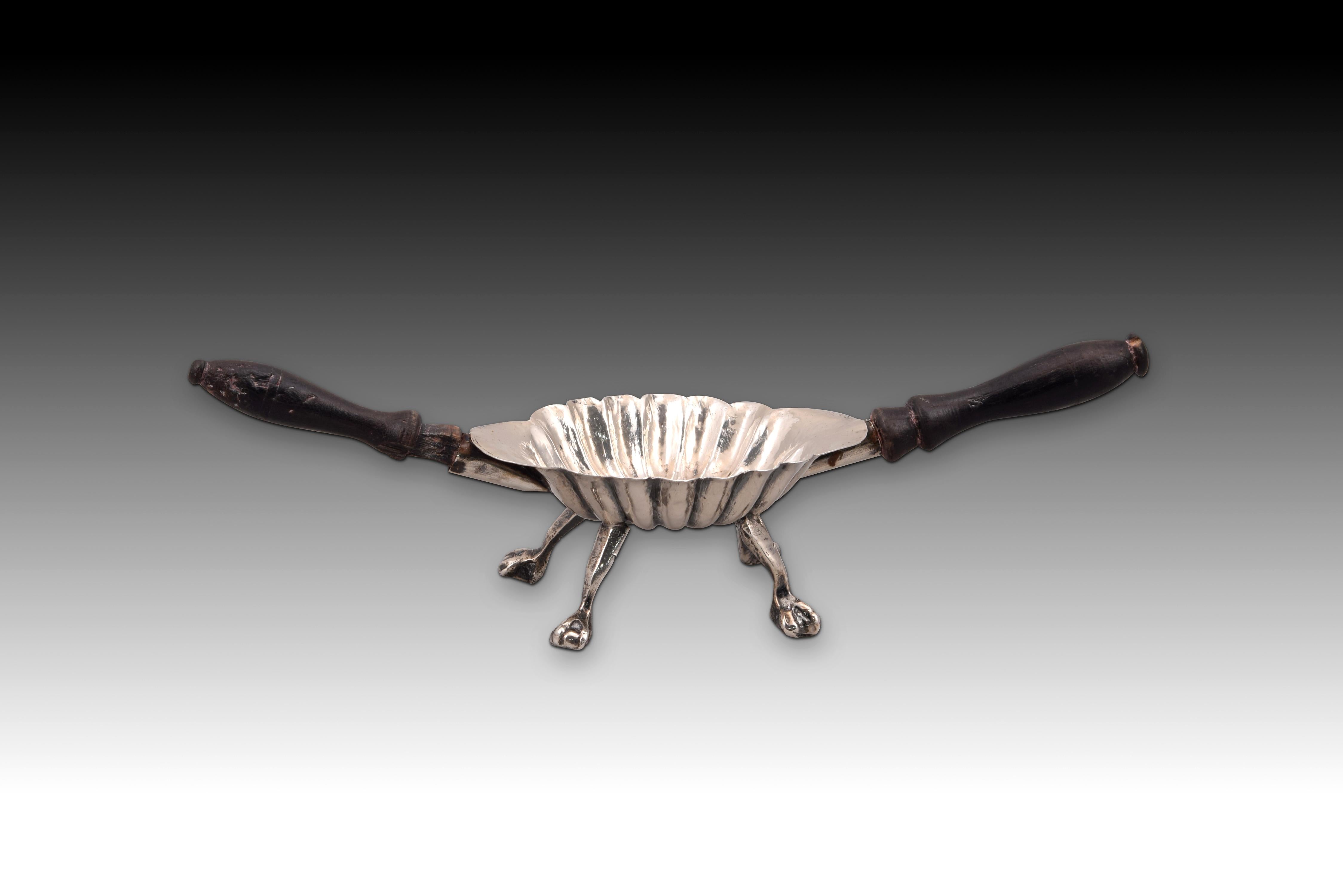 Gallon chofeta. Silver, Wood. XIX century. 
Oval chofeta with turned wood handles made in silver in its color that has a chevron or avenerado finish, as well as legs finished in a sphere with a claw. The lines and decorative elements of this piece
