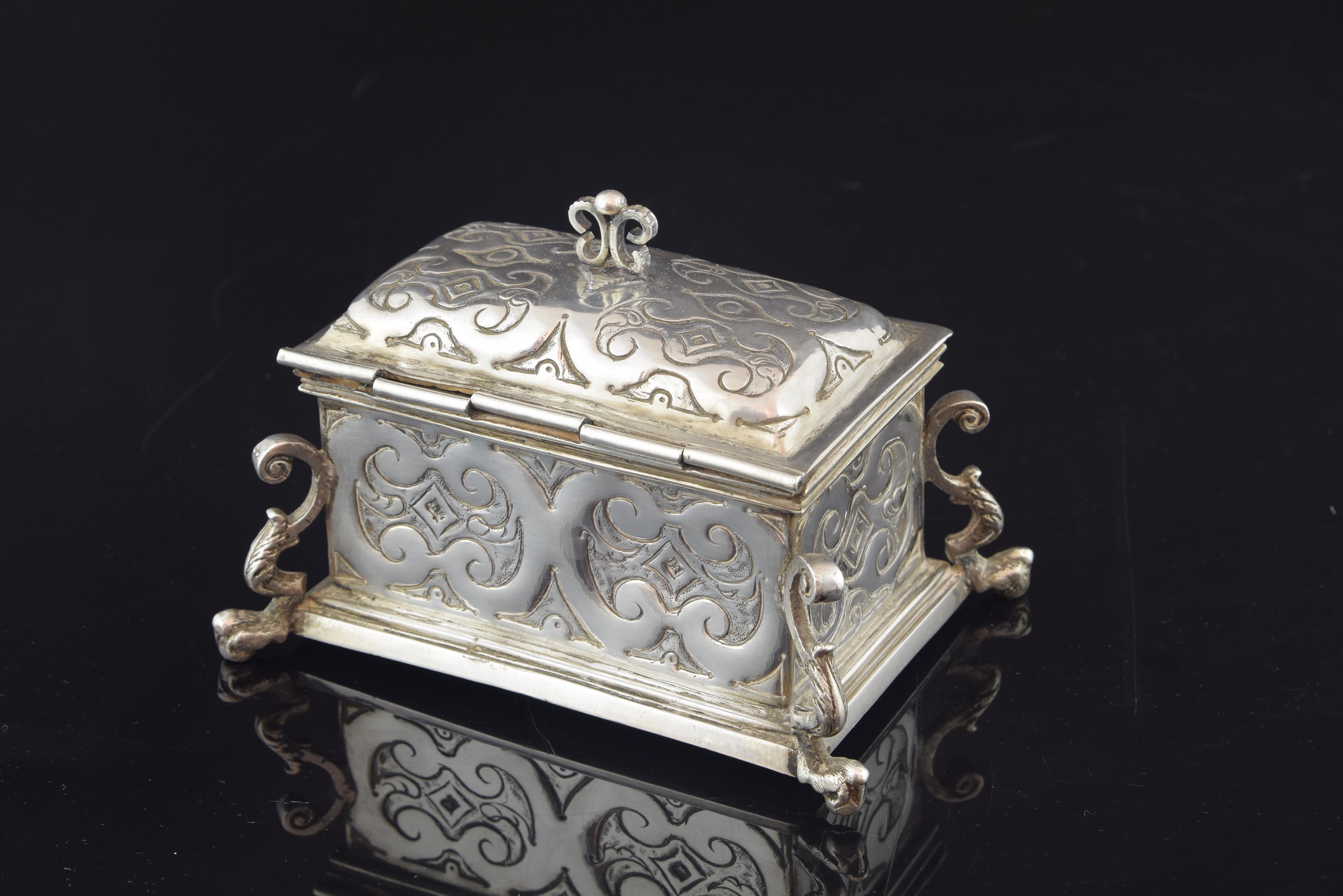 The silver box has elaborate legs, fixed in the corners of the same, which are a combination of volutes in C, plant elements and a lower end reminiscent of a claw. The rectangular body has a decoration embossed in light relief based on ribbons in ce