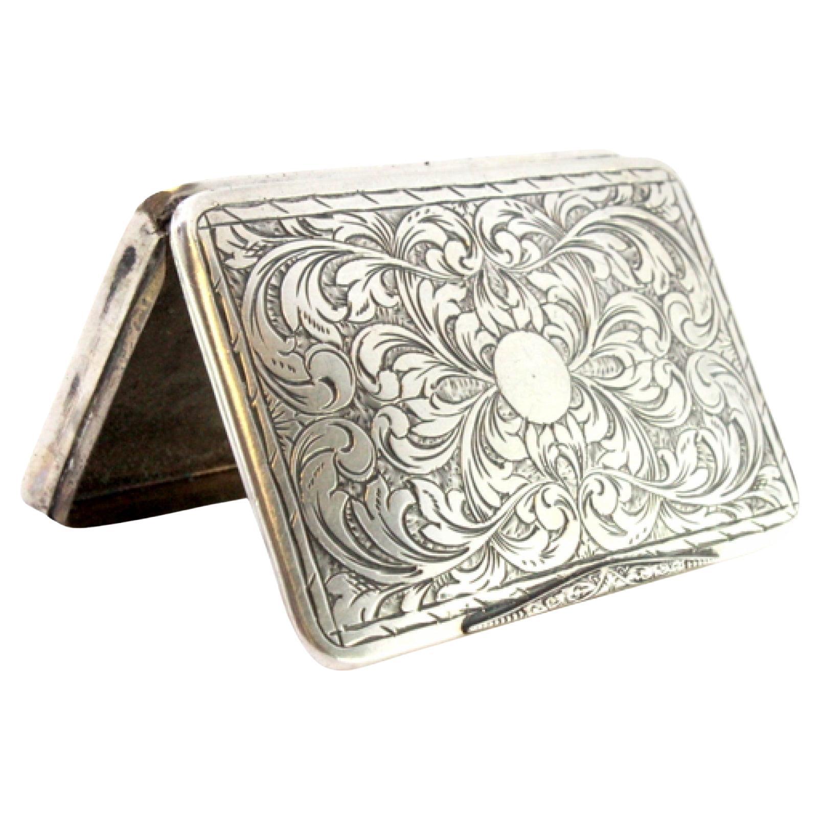Description: Silver snuff box with embossed floral motifs, monogrammed card, and hinged lid. Metal: Silver. Origin: European. Brand: Unknown. Weight: 36.86 grams. Dimensions: 7cm x 4.8cm. Content: 800/1000. Assay Mark: Yes. Additional information: