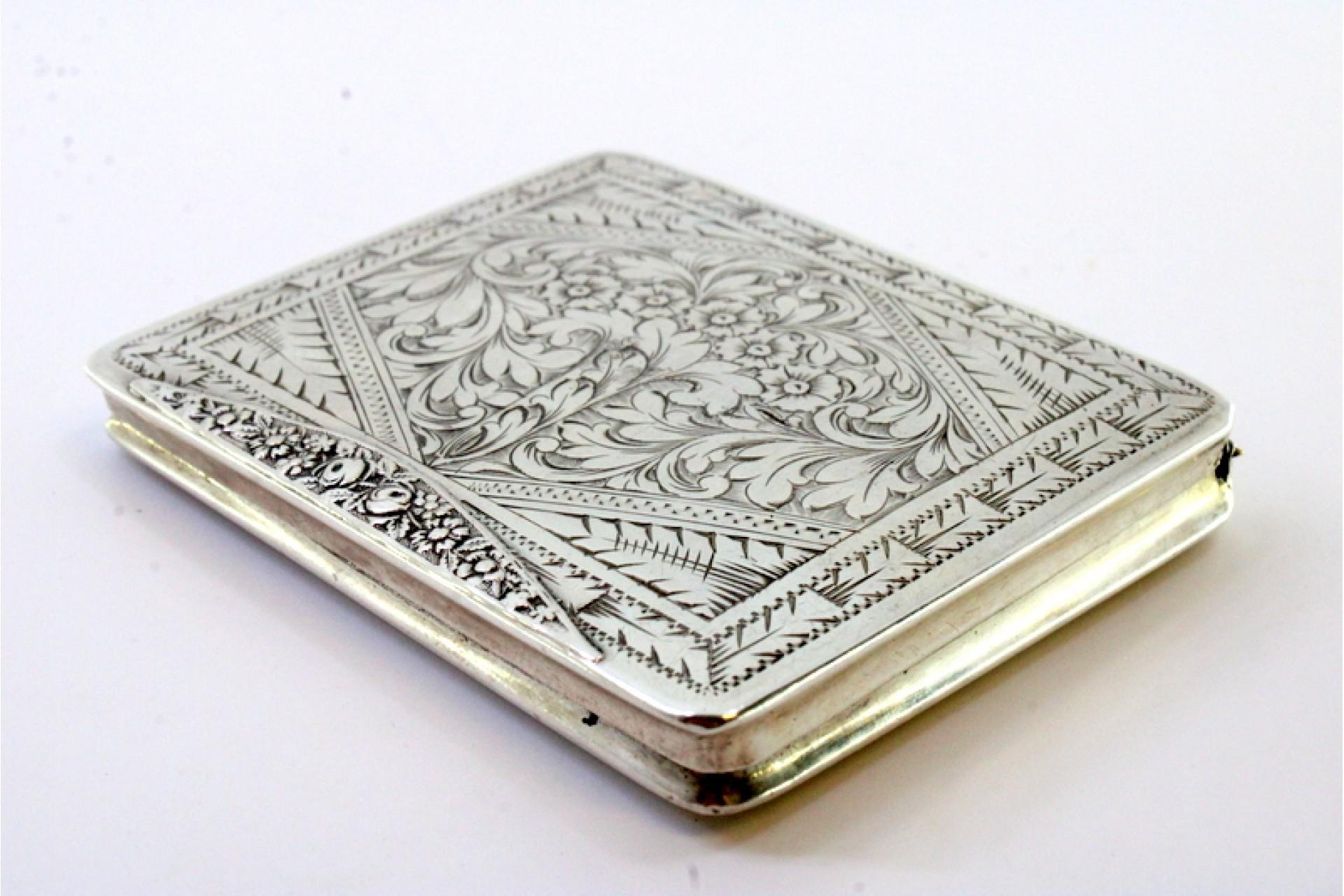 Description: Silver snuff box with embossed floral motifs surrounding a monogram card and hinged lid. Metal: Silver. Origin: European. Mark: Absent. Weight: 51.04 grams. Dimensions: 7.4cm x 5cm. Content: 833/1000. Assay Mark: Absent. Additional