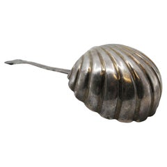 Silver soup ladle in the shape of a shell with grooves along the raised handle