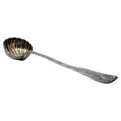 Silver soup ladle in the shape of a shell with grooves along the raised handle