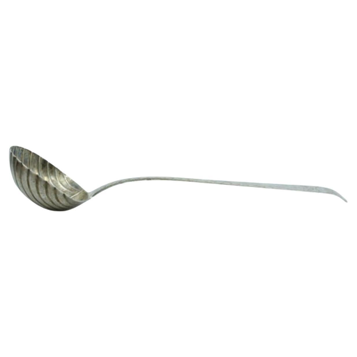 Silver soup ladle in the shape of a shell with grooves along the raised handle