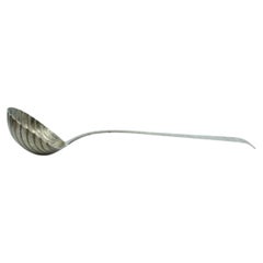 Silver soup ladle in the shape of a shell with grooves along the raised handle Silver soup ladle in the shape of a shell with grooves along the raised handle