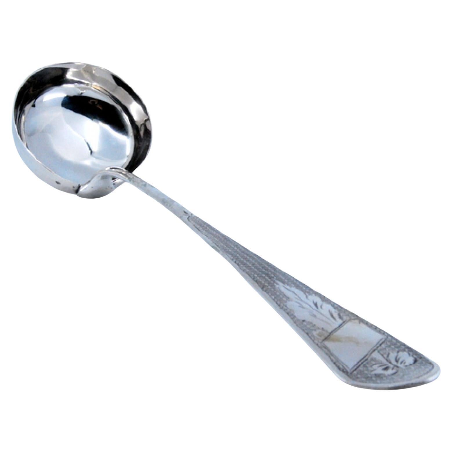 Silver soup ladle with engravings along the handle, including a monogram card