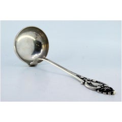 Silver soup ladle with grooves along the handle surrounding a monogram card
