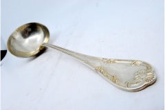 Silver soup ladle with grooves along the handle surrounding a monogram card