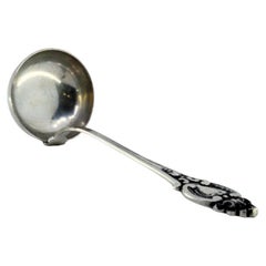 Silver soup ladle with grooves along the handle surrounding a monogram card