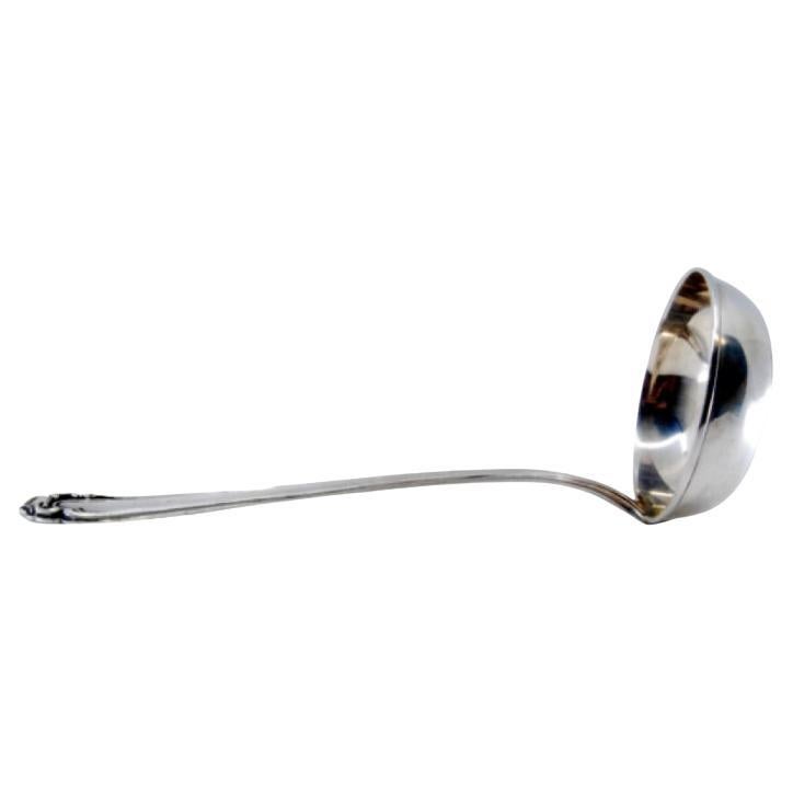 Silver soup ladle with grooves along the handle surrounding a monogram card
