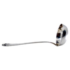 Silver soup ladle with grooves along the handle surrounding a monogram card