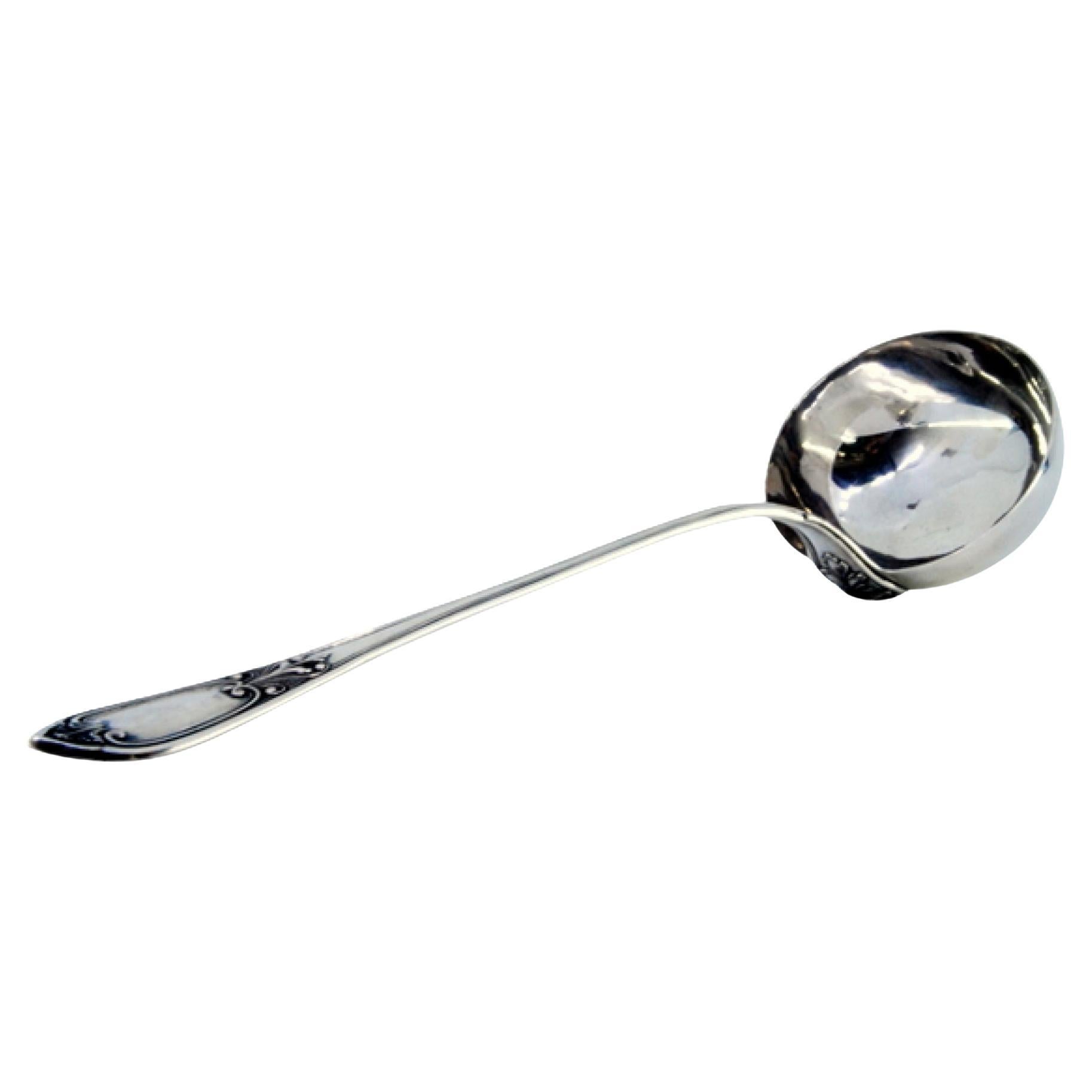 Silver soup ladle with reliefs along the handle surrounding a monogram card