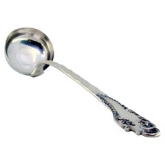 Silver soup ladle with wavy reliefs on the handle, surrounding a monogram card