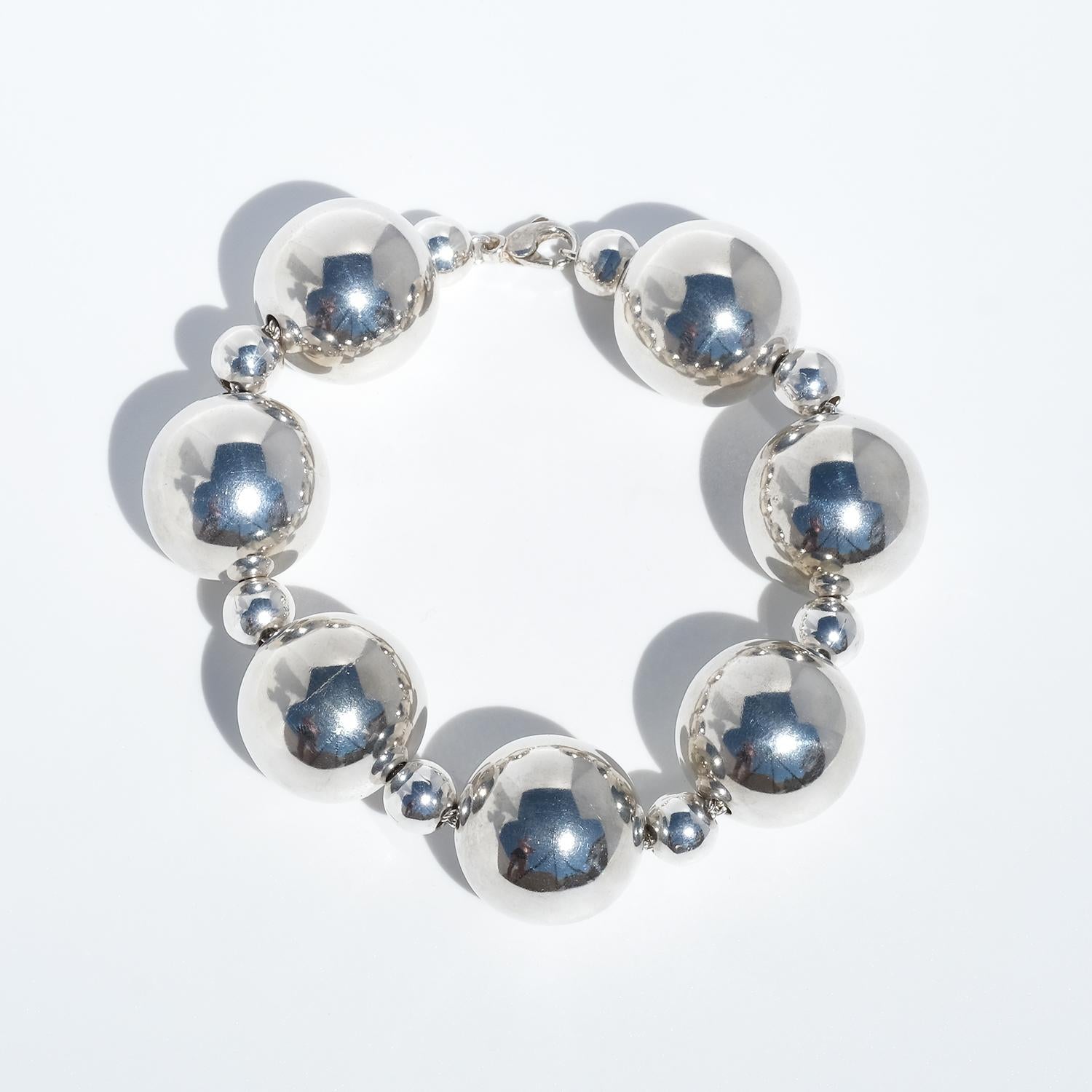 Esta pulsera, fabricada en Gotemburgo (Suecia) hacia 2016, presenta esferas de plata pulida grandes y pequeñas alternadas, engarzadas a lo largo de una cadena de plata visible que recorre toda la pieza. Cada esfera es hueca y muy reflectante, lo que