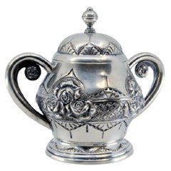 Silver sugar bowl w/ floral reliefs, double handle
resting on a frilled base