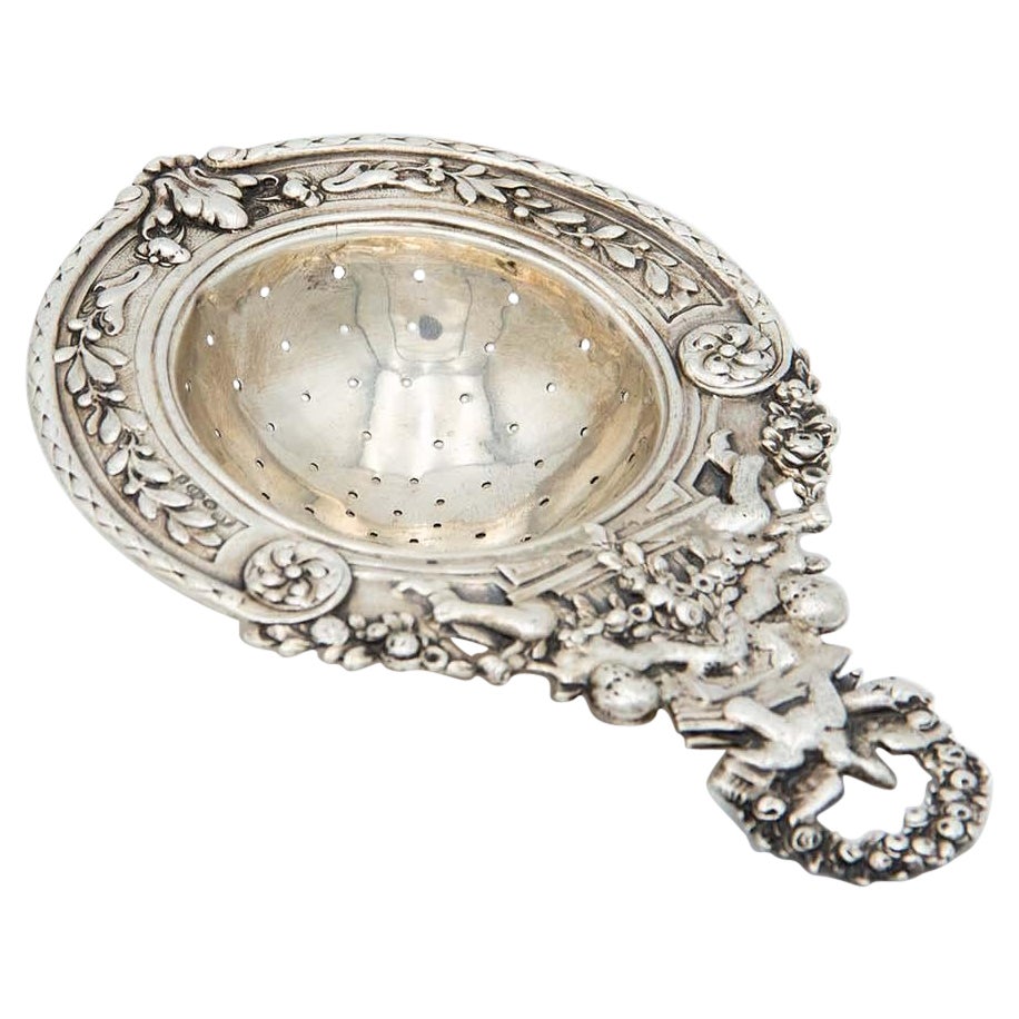 Silver tea strainer with embossed Puttis