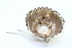 Silver tea strainer with raised plant motifs and hinged handle