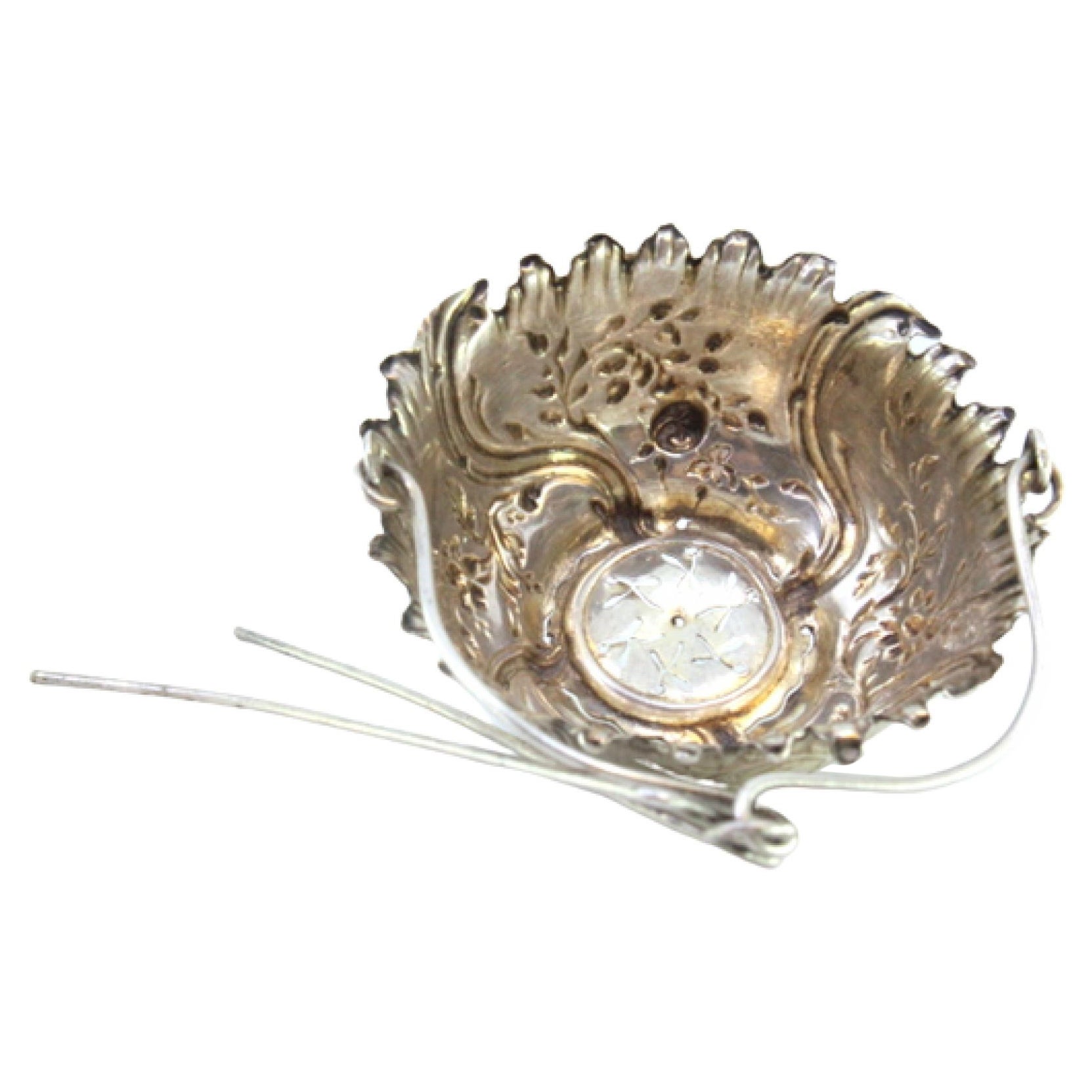 Silver tea strainer with raised plant motifs and hinged handle