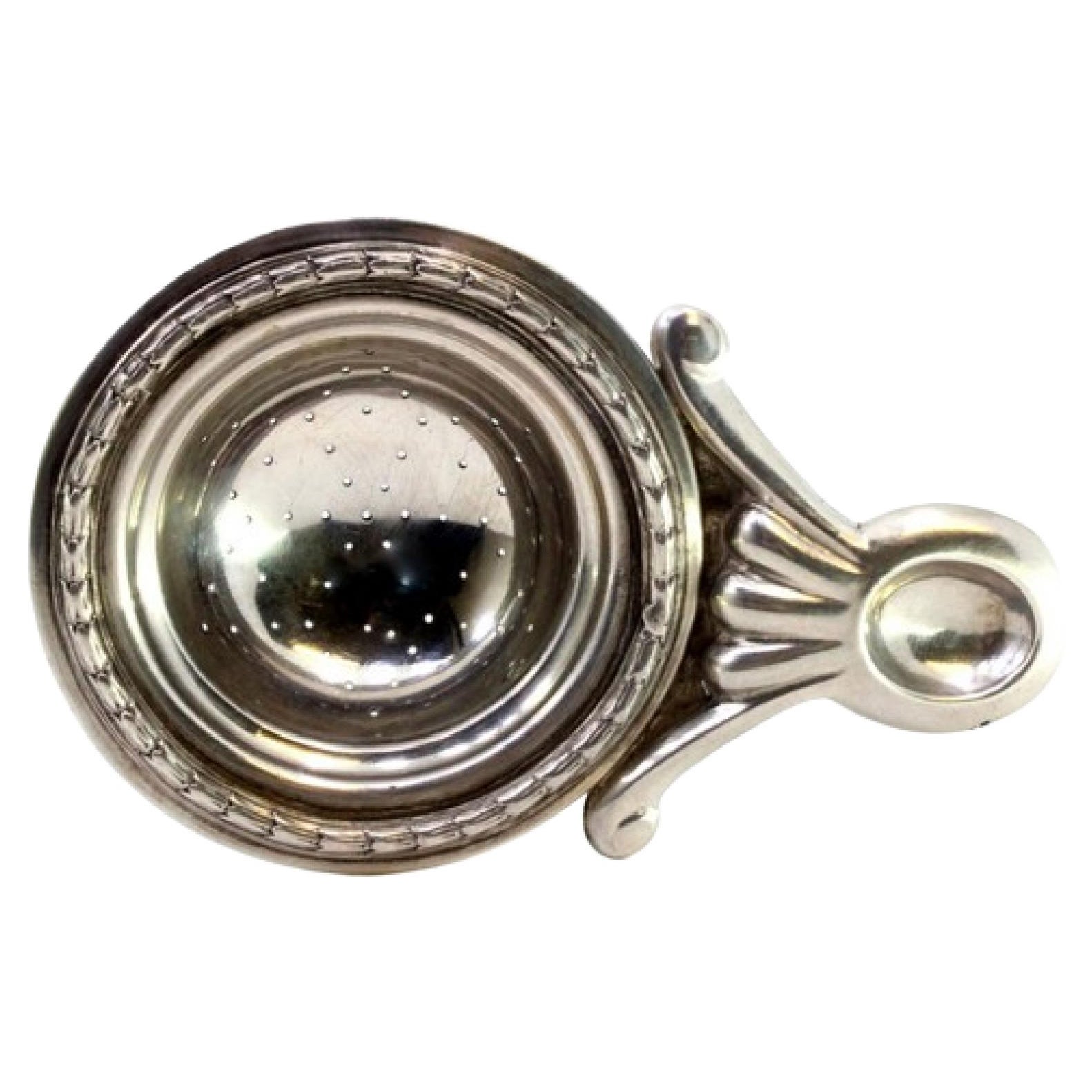 Silver tea strainer with reliefs and applications
