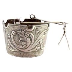 Silver tea strainer with reliefs, cut-out edge and hinged handle