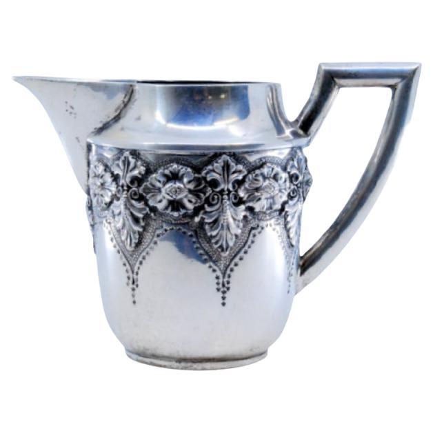Silberne Teekanne mit erhabenen floralen Motiven und geradem Henkel