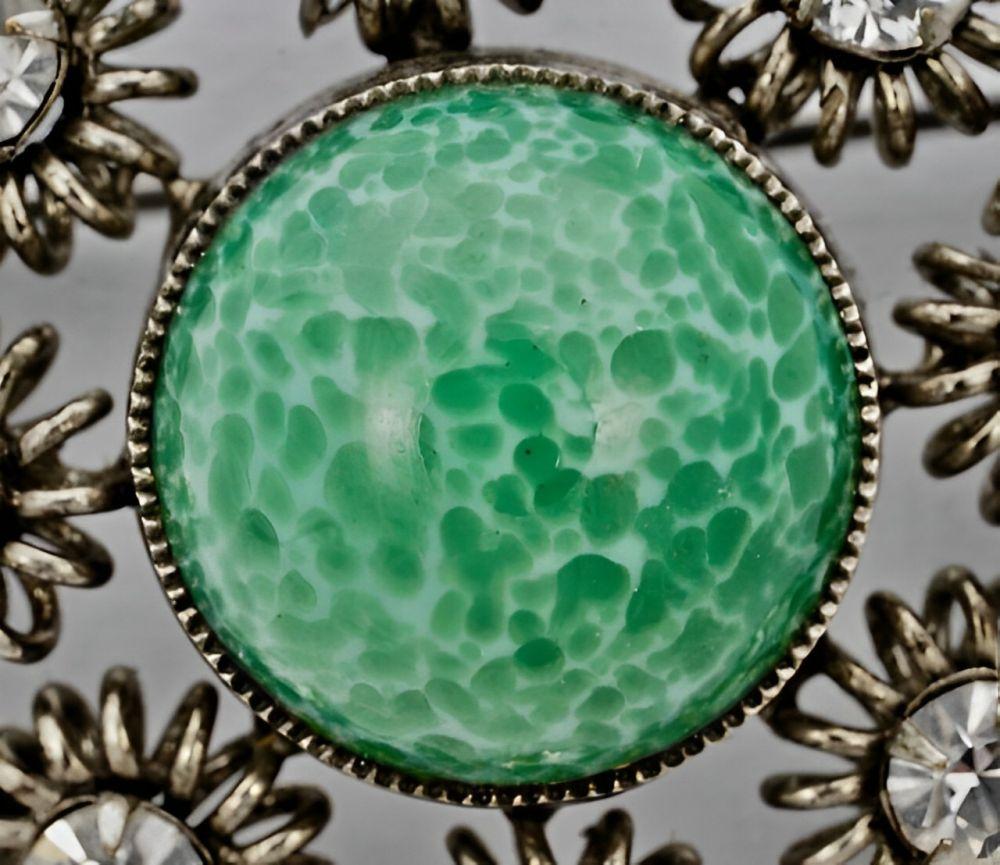 Wonderful round silver tone brooch featuring a beautiful speckled green glass stone. The green stone is surrounded by clear rhinestones in fancy settings and silver balls. Measuring diameter 3.5 cm / 1.37 inches.

This vintage brooch has such a