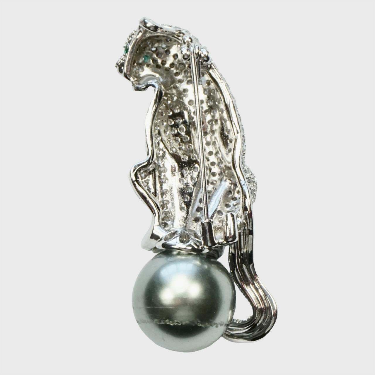 Fabuloso broche de pantera pavé en tono plateado con ojos facetados verdes, asentada sobre una perla de imitación gris. Tiene un pequeño gancho, quizá para una cadena. La perla tiene arañazos y algo de movimiento.

Mide 5 cm de largo por 1,9 cm de