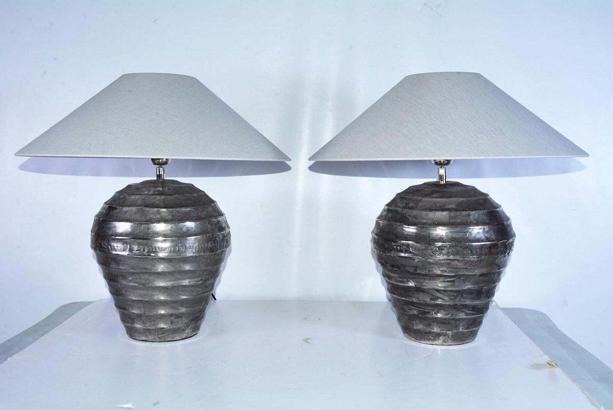 Silver colored metal lamps from India with Belgium linen coolie style shades. The jar shaped lamp has hammered surface with ribbed trimmed details encircling the body. Hollywood Regency Indian style ginger jar form table lamps with ethnic