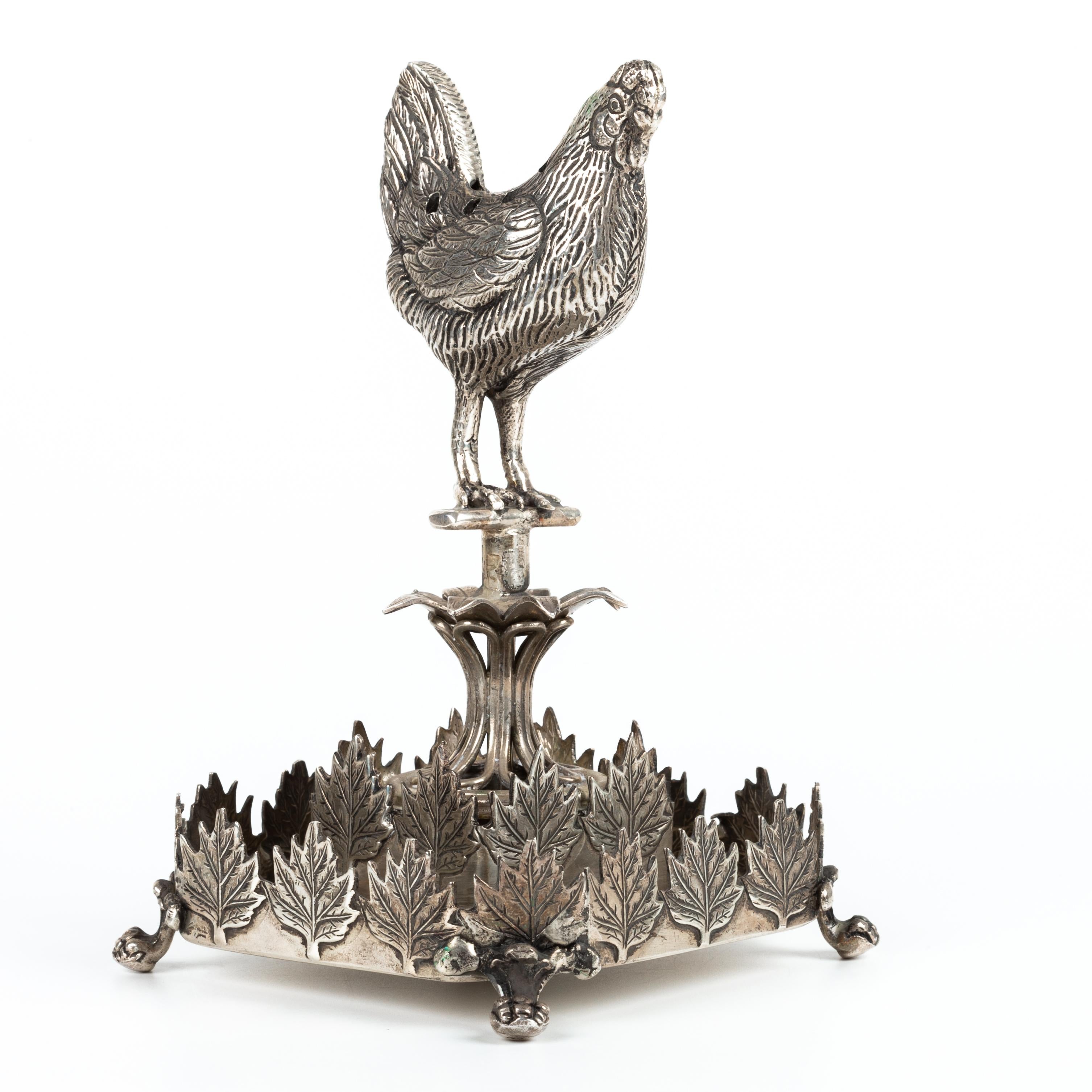 Porta stuzzicadenti a forma di gallina in argento portoghese, con marchio 925/1000 e aquila; decorazione in rilievo con motivi vegetali; base quadrata con quattro gambe a forma di voluta. Peso: 255,4 grammi. Dimensioni: 13,5 cm. In buone condizioni.