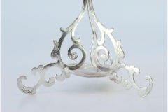 Silver toothpick holder with cutouts and curls and a plate at the base