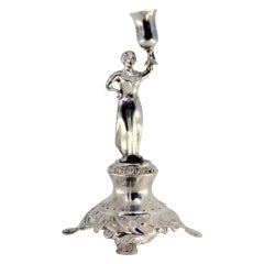 Silver toothpick holder with lady holding cup on raised base with three feet