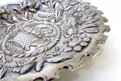 Silver tray w/ cutouts on the edge & basket w/ fruit surrounded by spun flowers