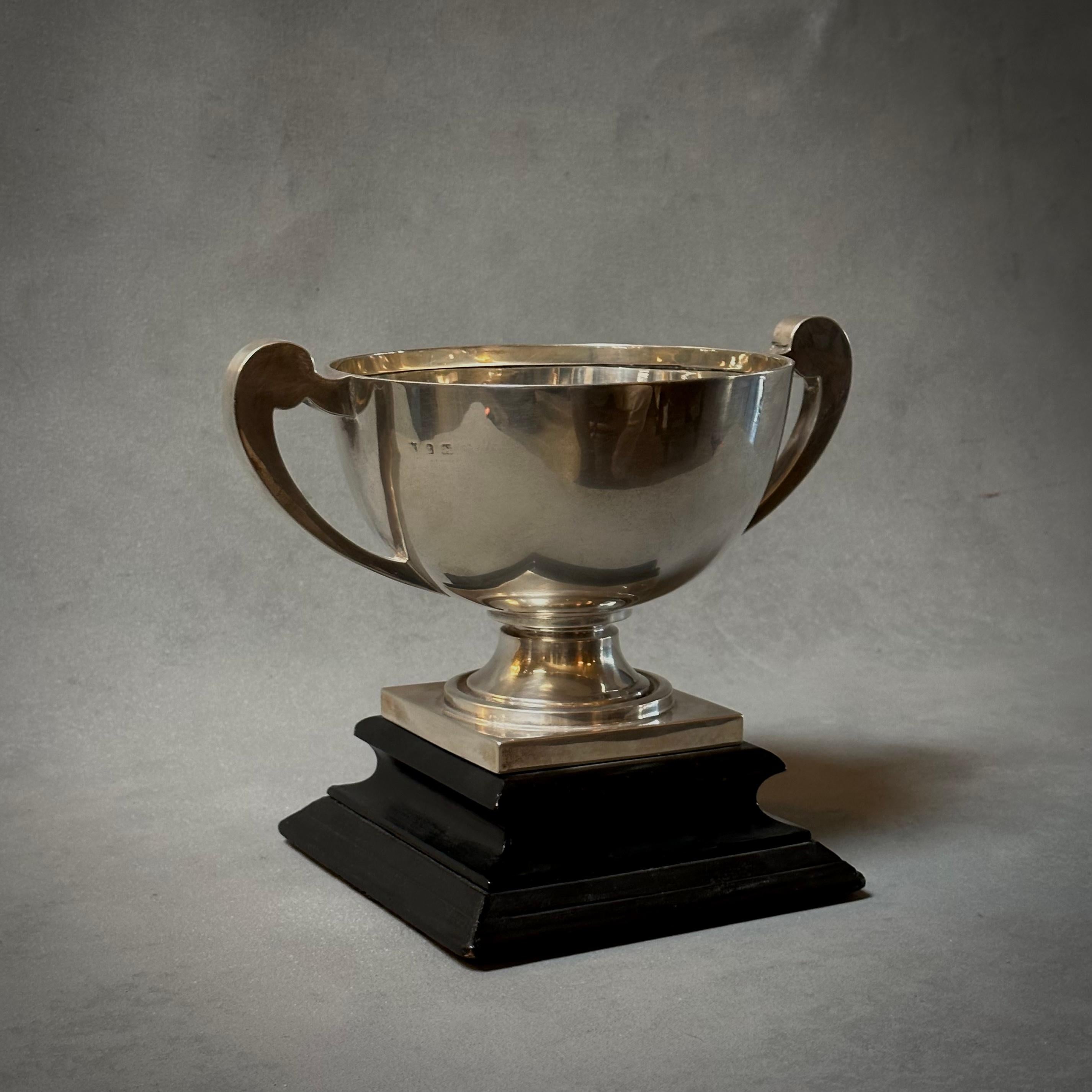 Silver trophy cup mounted on an ebonized beveled wood base with simple bowl shape and gracious neoclassical accenting. An easy way to elevate any shelf or tabletop with a touch of traditional polish. 

England, circa 1900

Dimensions: 10.5W x 7D