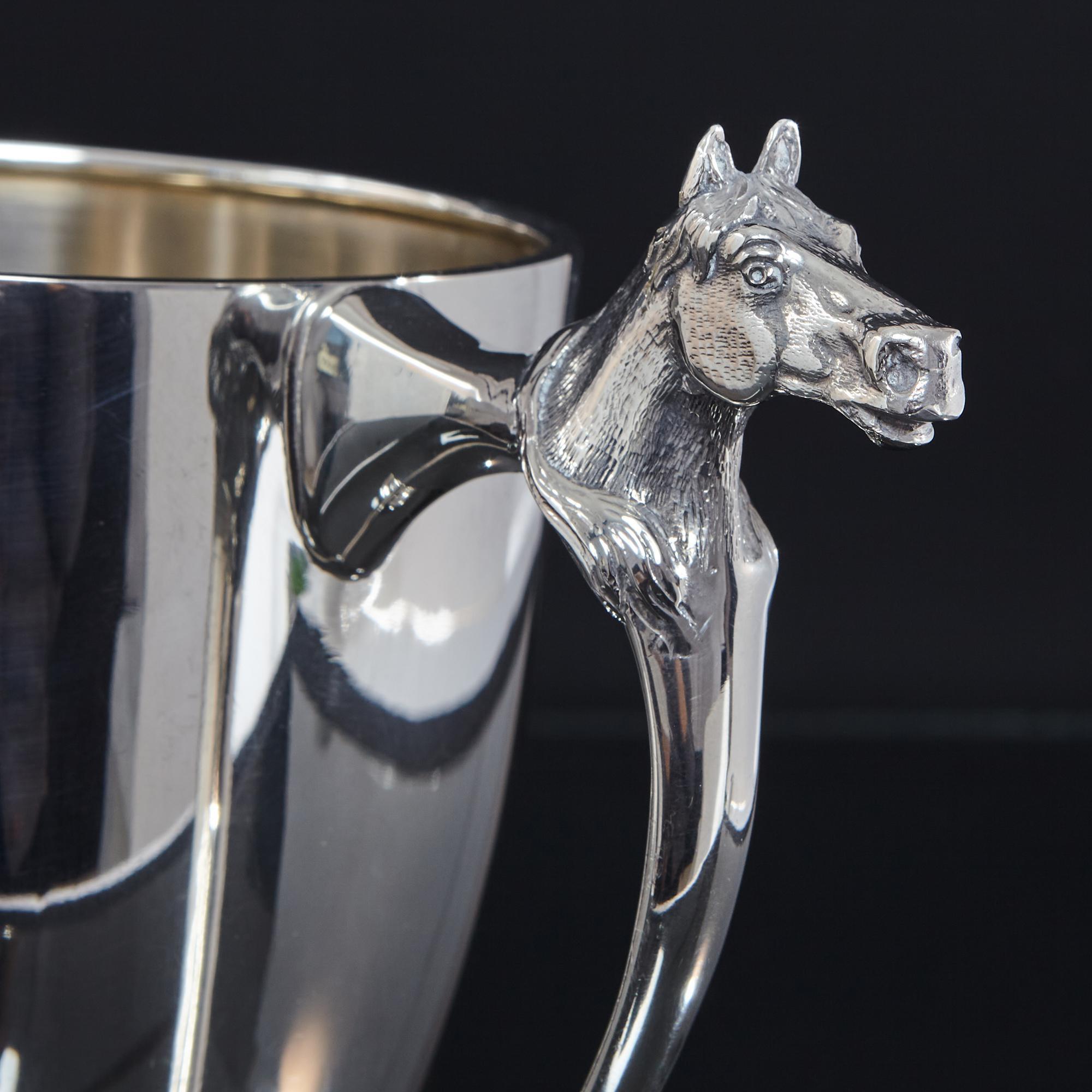 A two-handled silver trophy cup of equine interest. This early 20th century silver cup is of a particularly good gauge of silver creating a tremendously heavy piece and is decorated with two cast horse head mounts on the handles. Suitable for