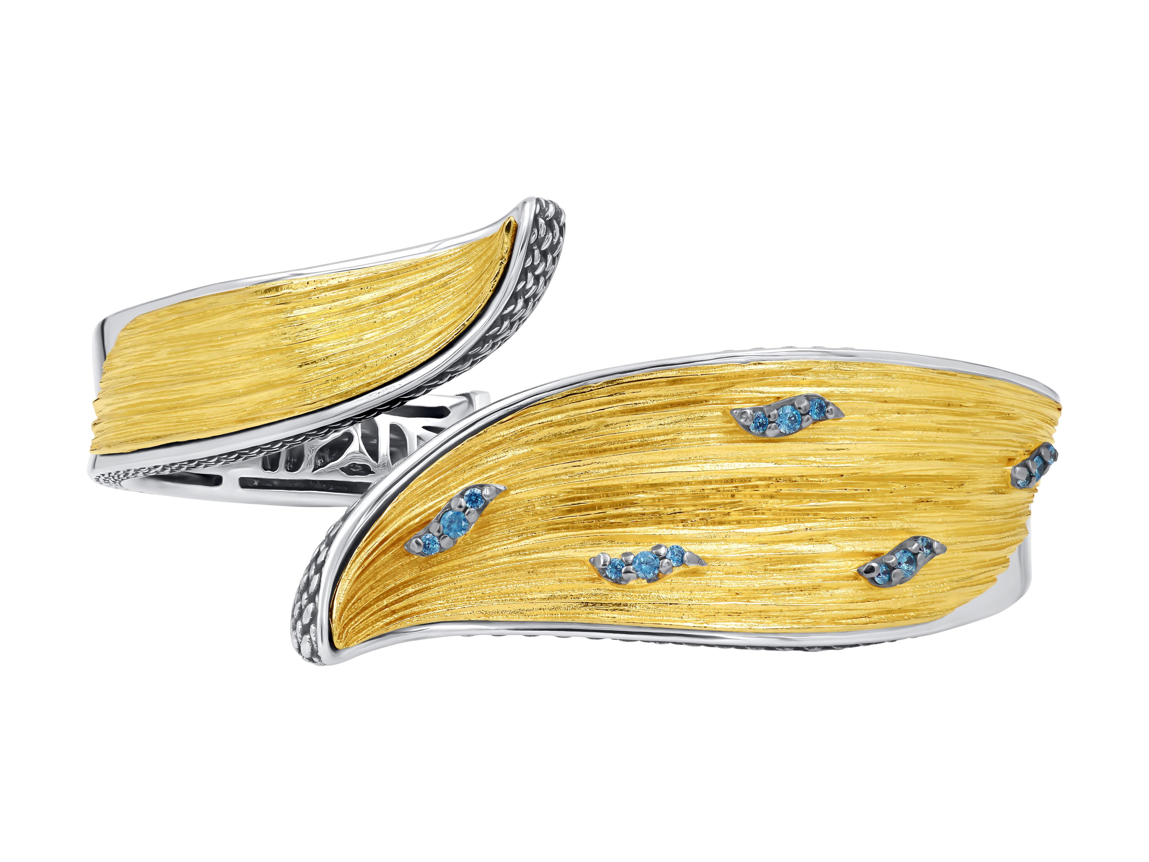 Silver two-tone bangle bracelet with gold plated textured surface and adorned with blue topaz stones. This stunning piece of jewelry combines the elegance of silver with the beauty of blue topaz to create a unique and eye-catching design.
The