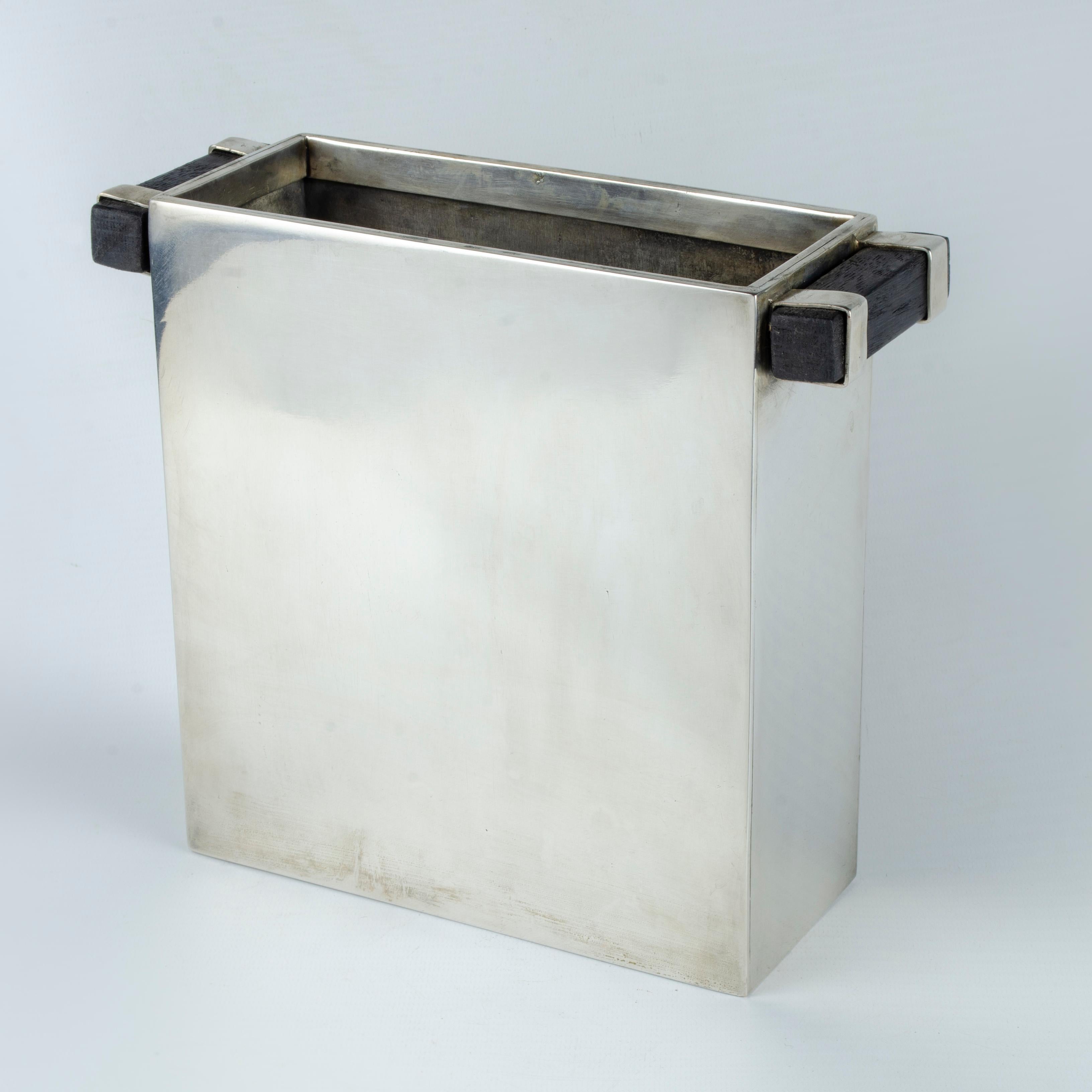Vase rectangulaire, en métal argenté avec des poignées en bois, conçu par la Maison Desny Paris (1927-1933). Il a été produit en différentes tailles. Un de ces spécimens est exposé dans le 