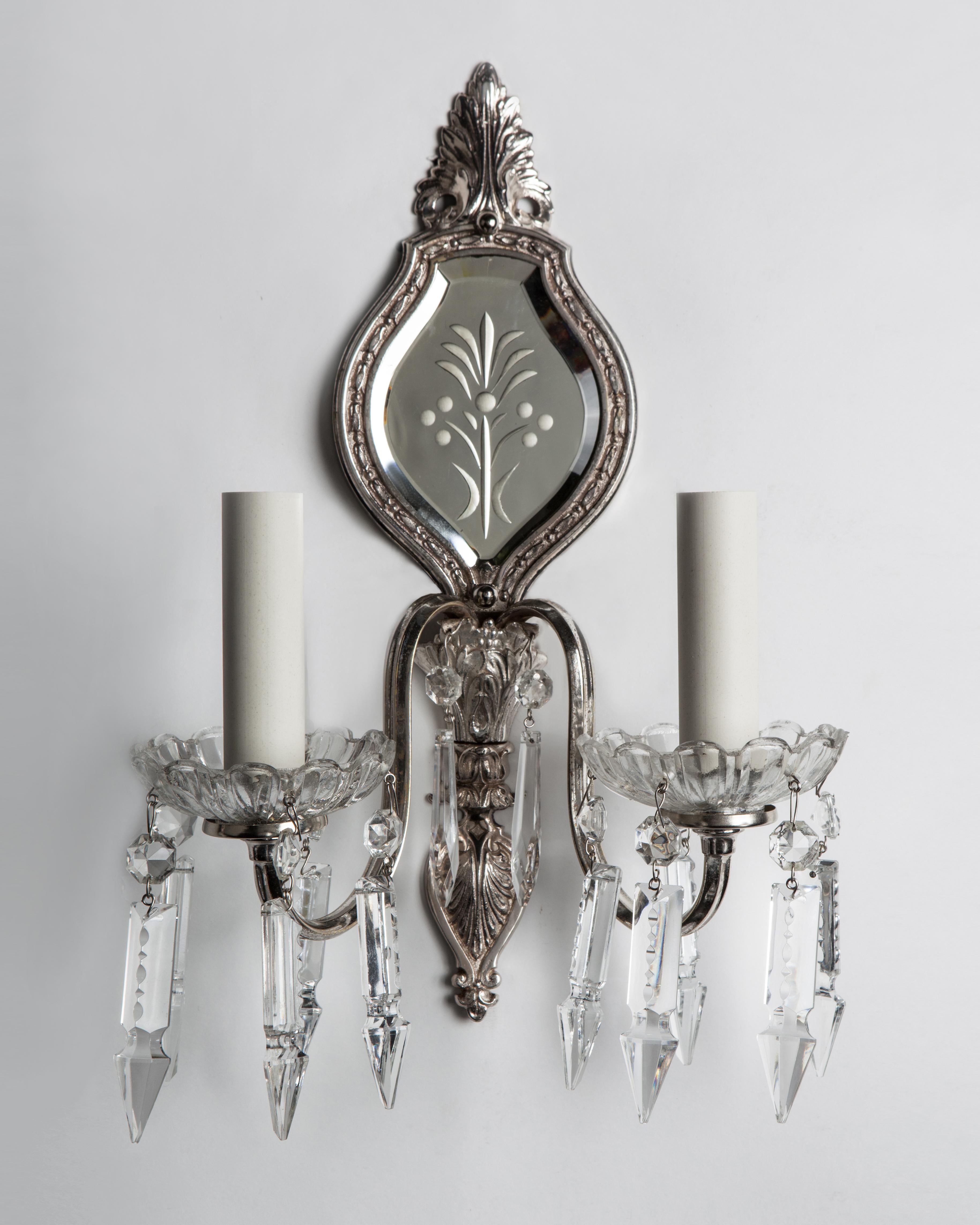 AIS2929
A pair of two arm sconces with wheel-cut mirrored backplates, dressed with crystal bobeches and spear prisms. In their original aged silverplate finish. Due to the antique nature of these fixtures, there may be some nicks or imperfections in