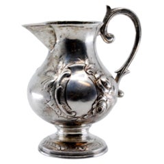 Silver wine jug with engraved floral motifs surrounding a monogram card