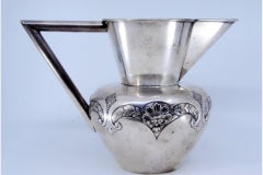Silver wine jug with raised plant motifs and smooth angular handle