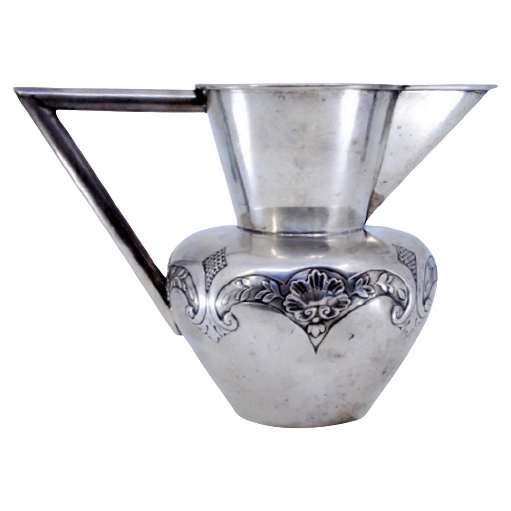 Silver wine jug with raised plant motifs and smooth angular handle