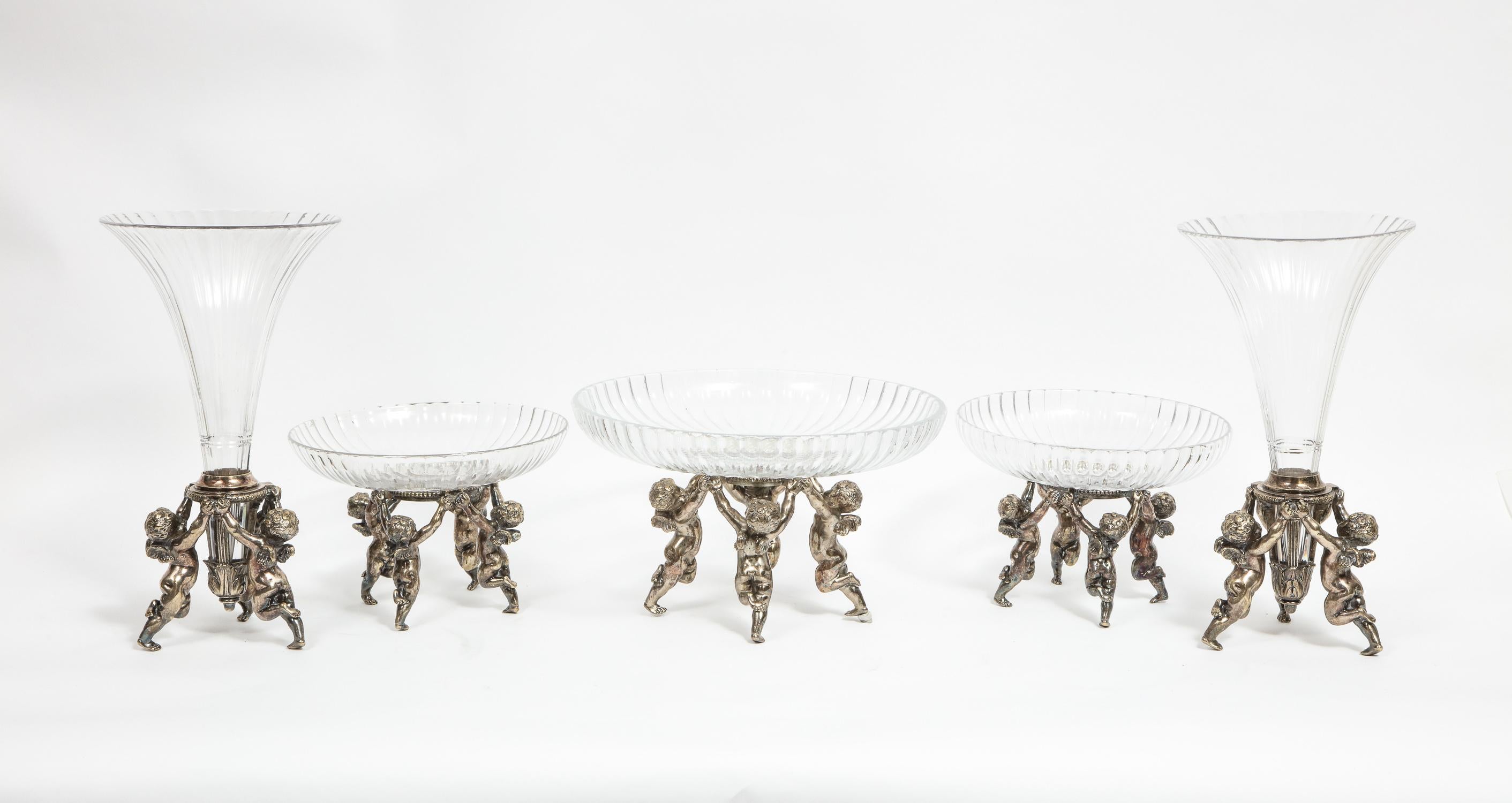 A French silvered bronze and cut glass five-piece table garniture centerpiece
Attributed to Baccarat, Paris, circa 1880.

Comprising: 
A pair of silvered bronze trumpet vases with putti and original cut glass vases
A pair of tazza centerpieces