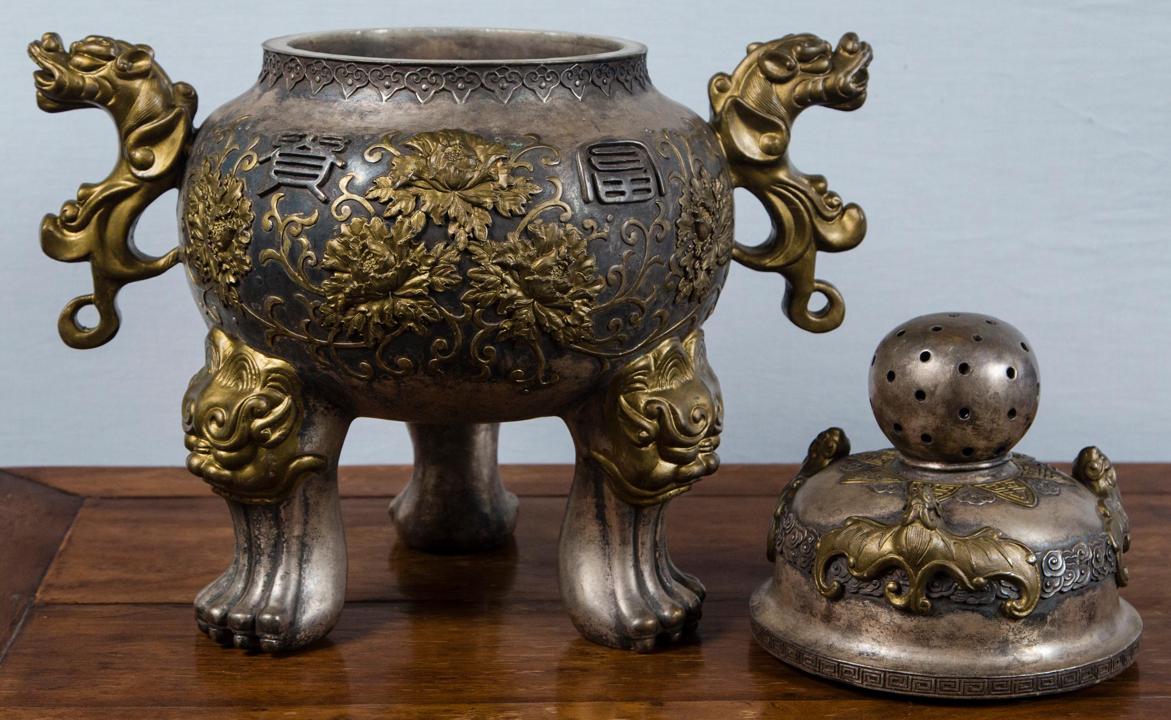 Removable pierced lid. Decorated with bats, cartouches of chrysanthemums, dragon head handles and animal masks above paw feet. Those elements may have been gilded at one time, but now painted gold.
From handle to handle measures 19 inches.