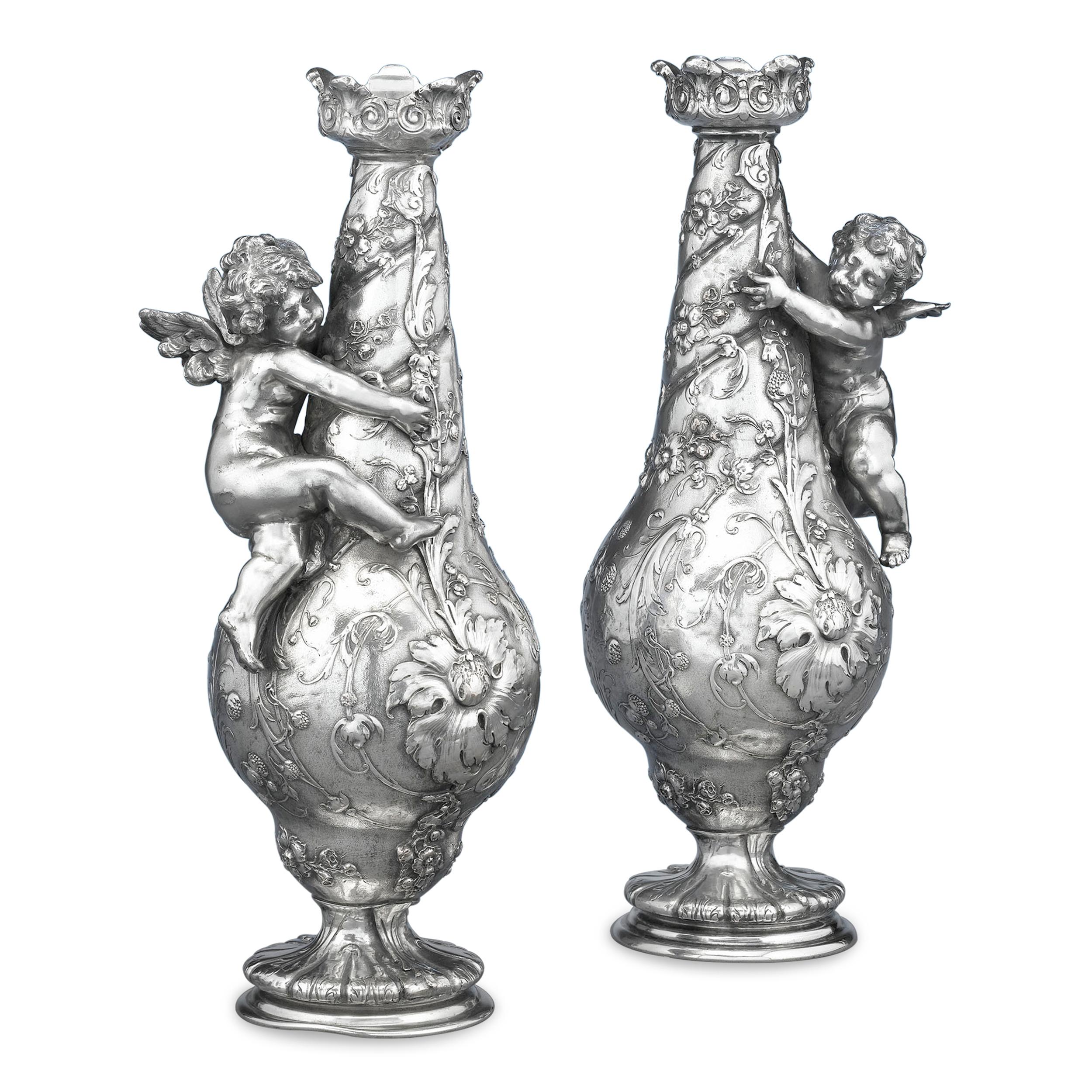 Winged cupids cling to these marvelous silvered bronze vases. Crafted in the neoclassical style, the vases also display a hint of the Arts and Crafts aesthetic, as they resemble a pair of luscious and naturalistic pears, each draped in flowering