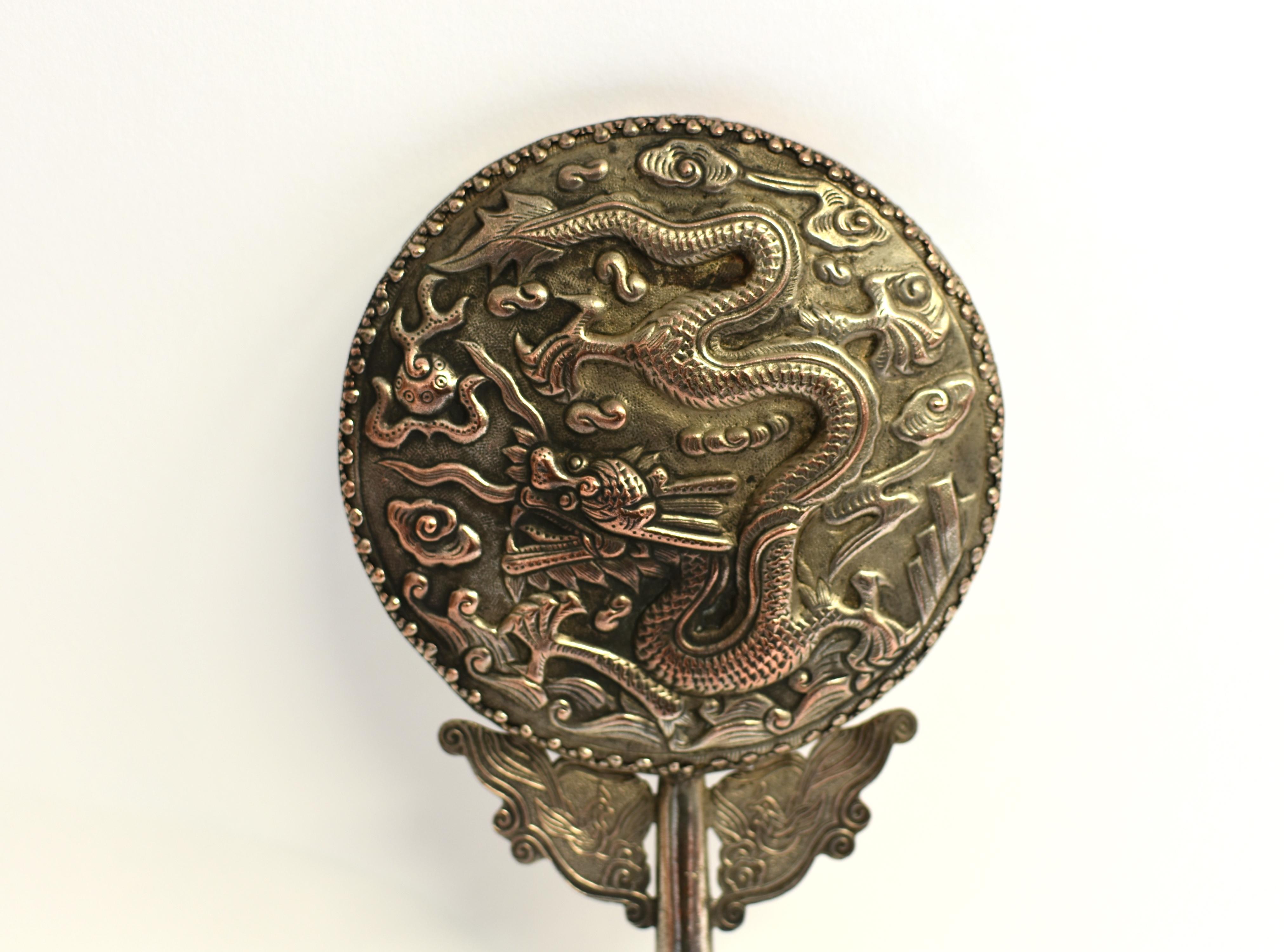 A beautiful hand held mirror with silvered metal depiction of dragon flying in the auspicious cloud above ocean waves. The dragon with curved body and fully opened talons chasing a fire ball, mouth wide open and eyes bulging, all conveying power and